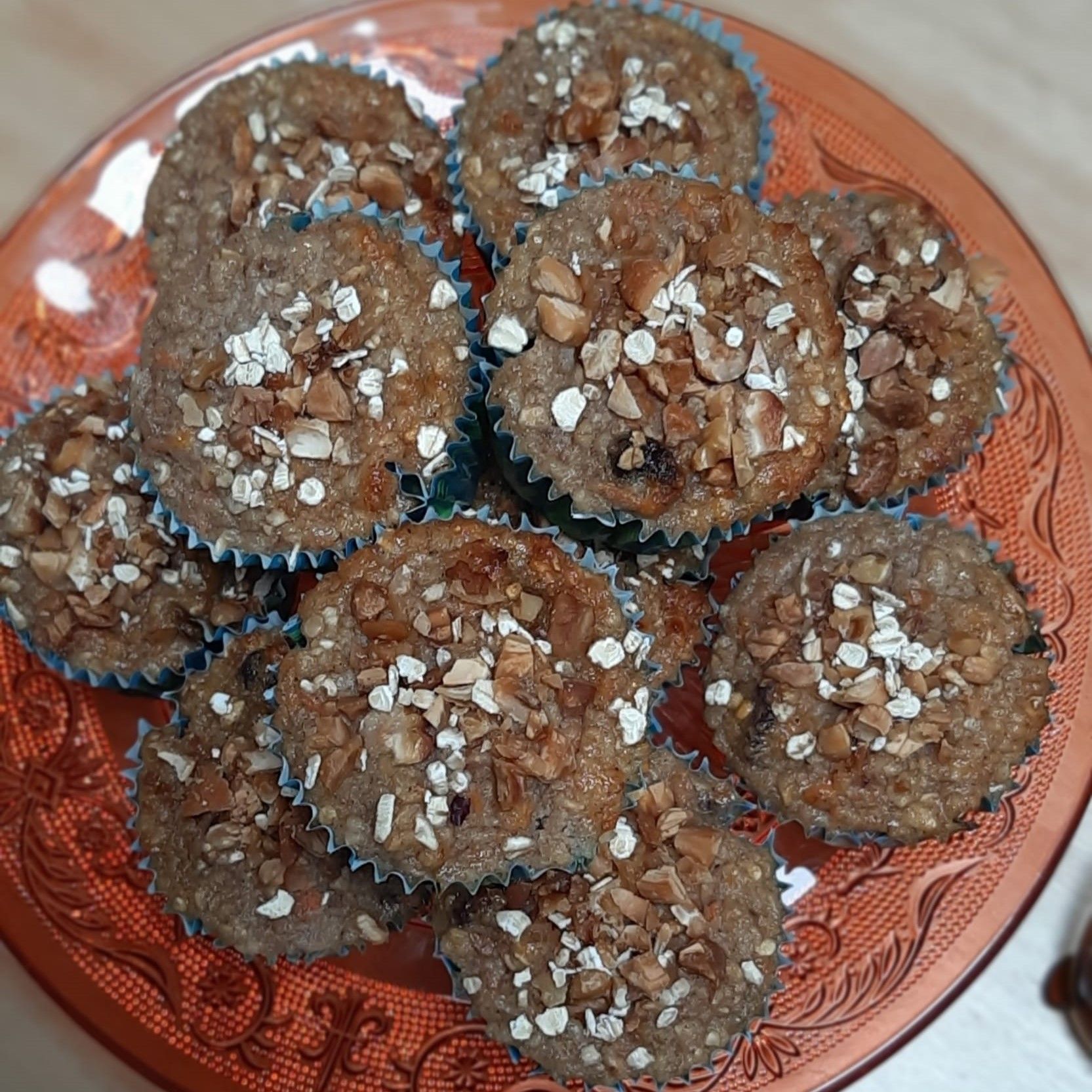 Muffins op een oranje bord, bedekt met havermout en noten. Ze zitten in blauwe cupcakevormpjes.