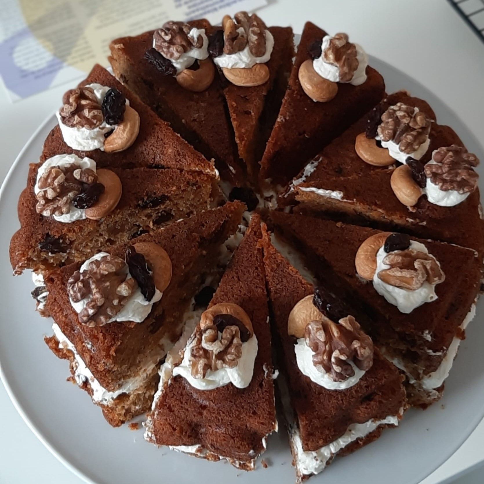 Gesneden worteltaart met slagroomglazuur, walnoten en cashewnoten op een wit bord.
