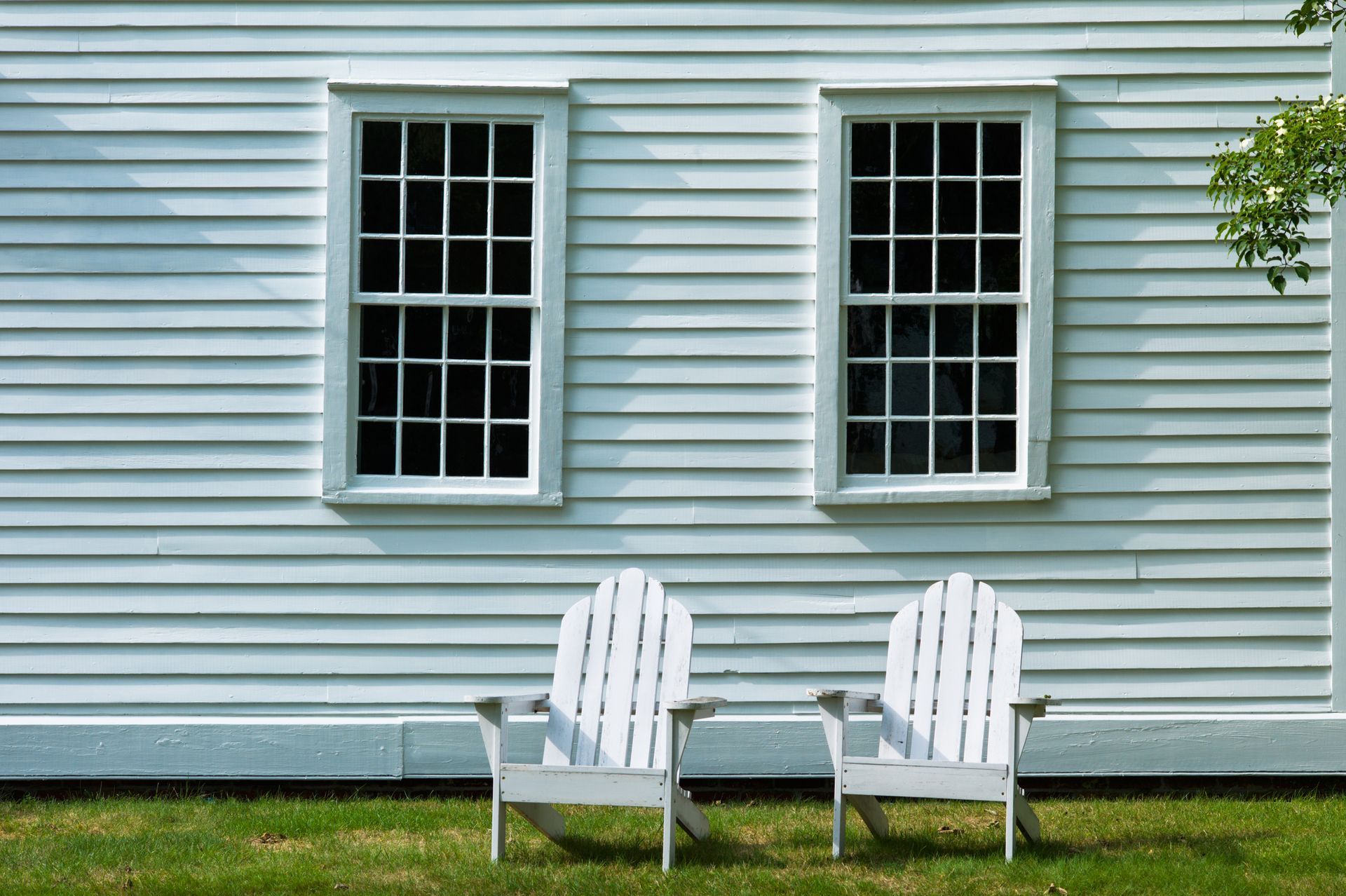 Two white lawn chairs are sitting in front of a white house.