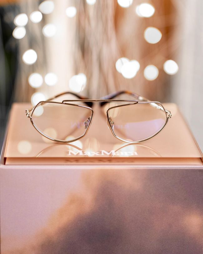 Gold wire-frame glasses on a rose-gold box with blurred lights in the background