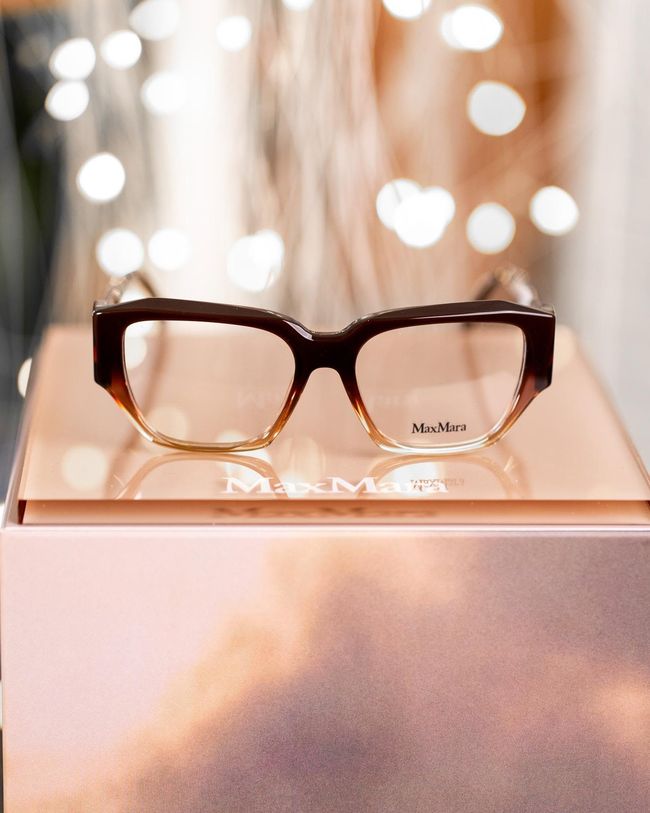 Brown eyeglasses on a rose-gold display box with soft bokeh lights in the background