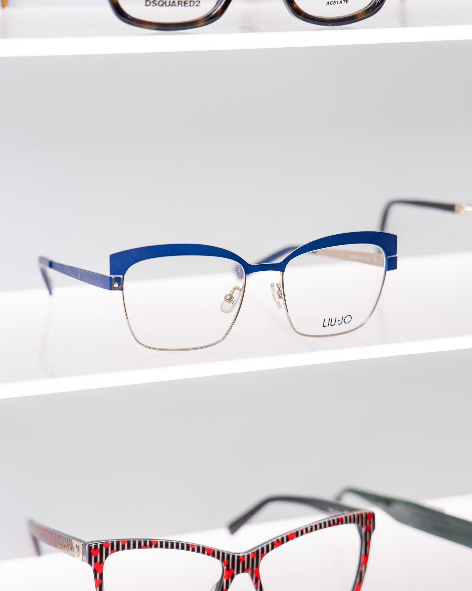 Blue and clear eyeglass frames on a display shelf, with red patterned frames below
