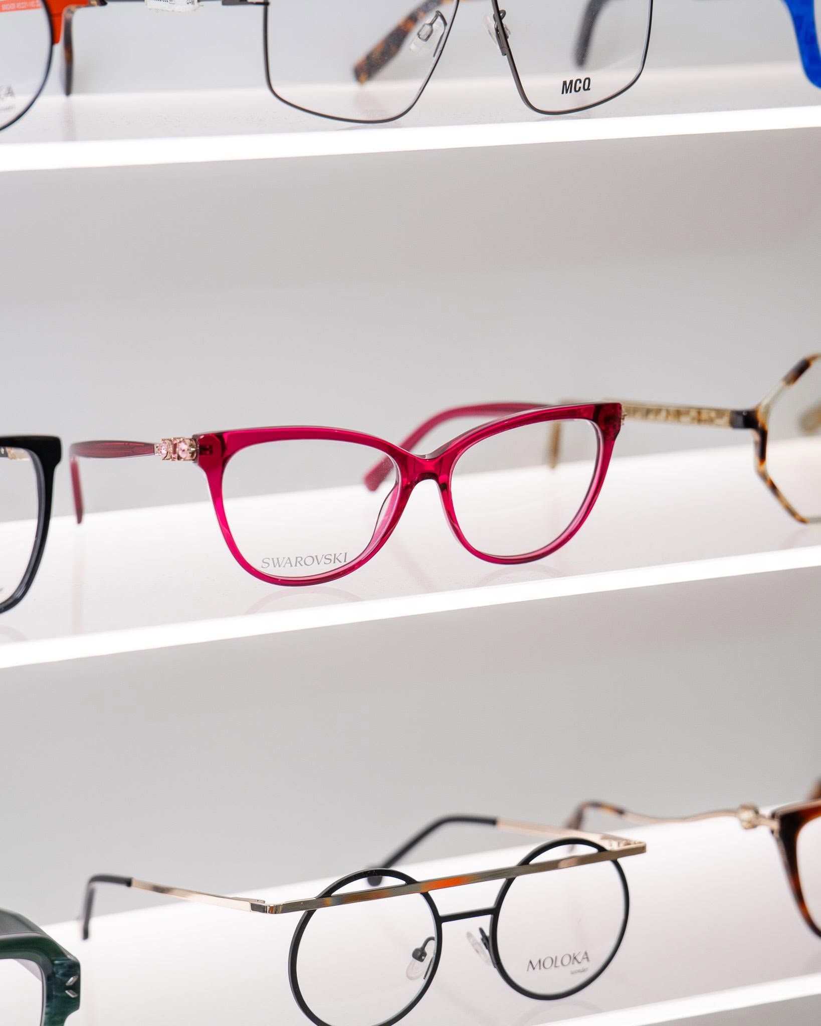 Rows of eyeglasses on a white display, including pink, black, and gold frames.