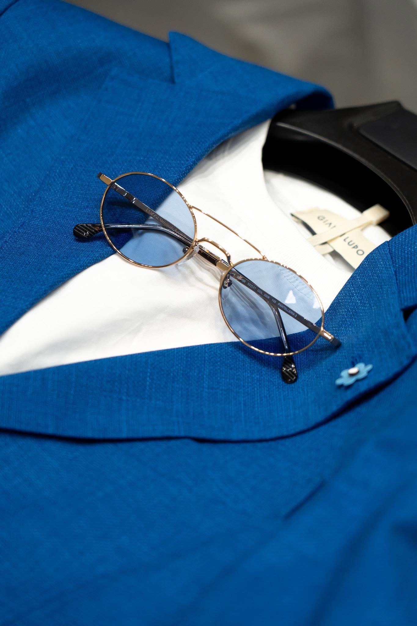 Gold-rimmed glasses on a blue shirt beside a black tie and white collar
