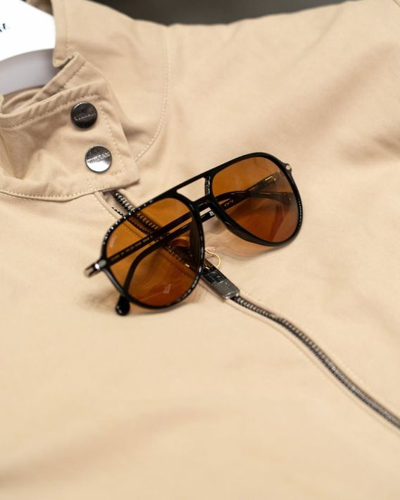 Black-framed amber sunglasses on a beige shirt with silver snaps and a zipper pull cord