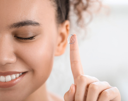 Close-up of a smiling woman applying clear skincare cream to her fingertip