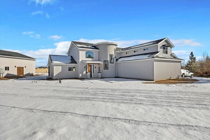 Light gray house with snow-covered ground and a clear blue sky.
