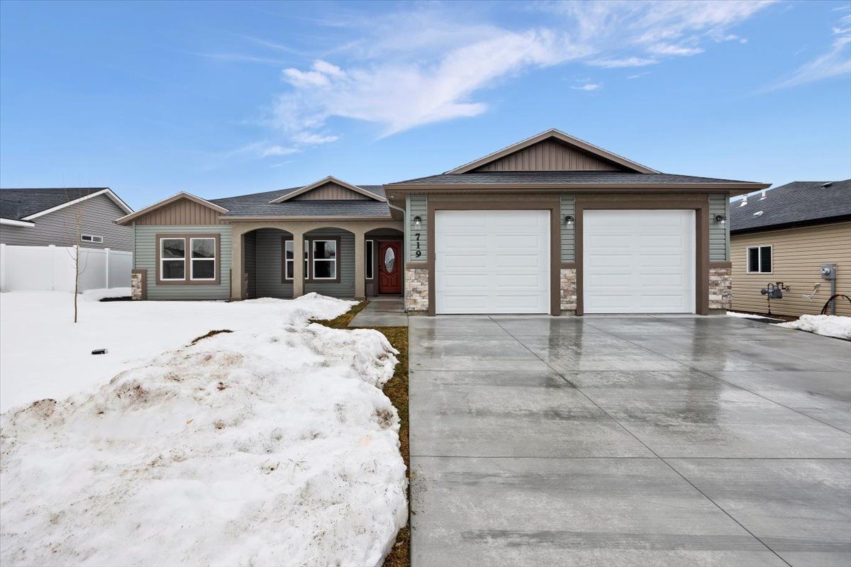 Residential house with a two-car garage, snow on the front yard, and a clear sky.