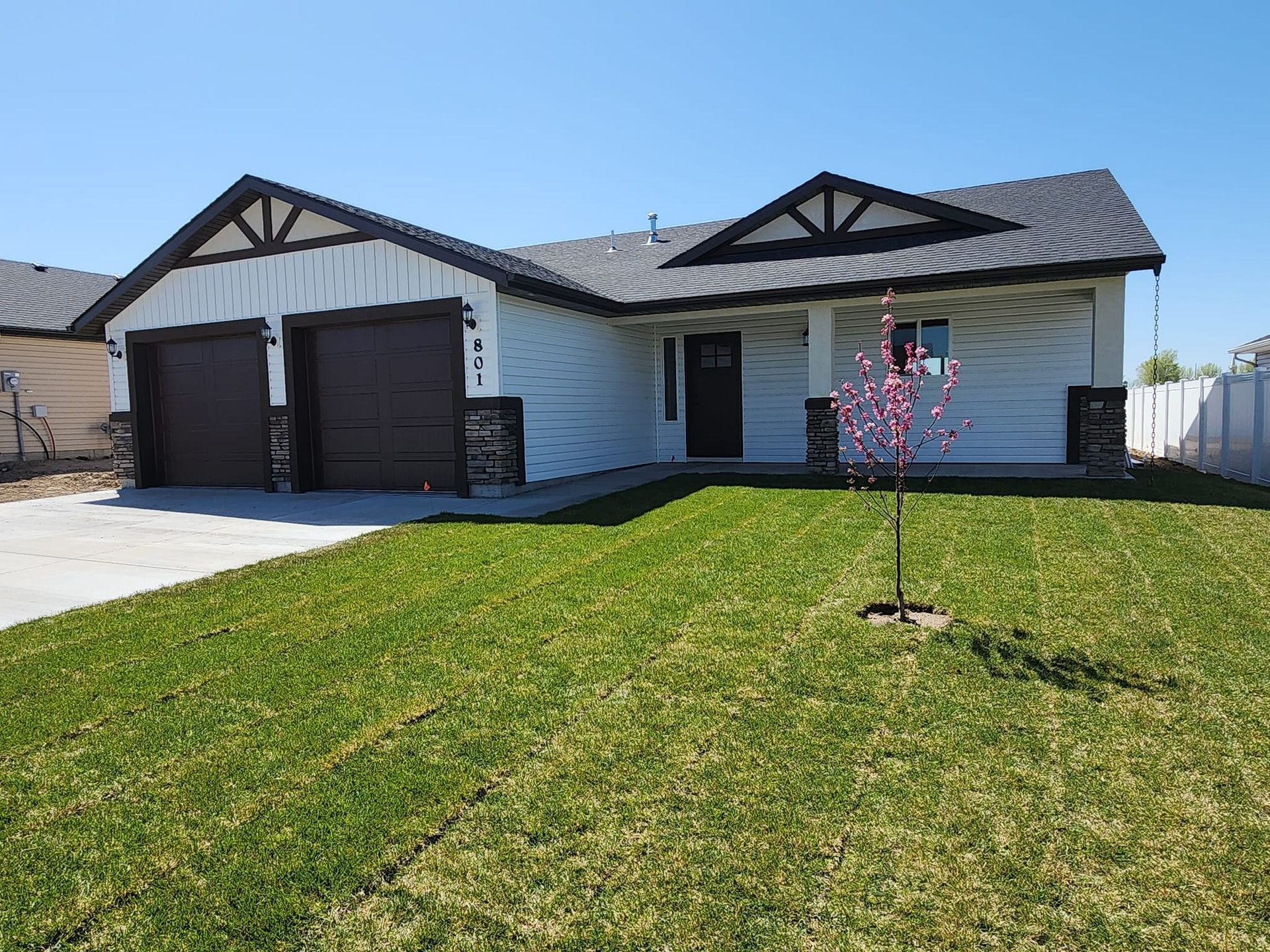 White house with black trim, two-car garage, and green lawn under a blue sky.