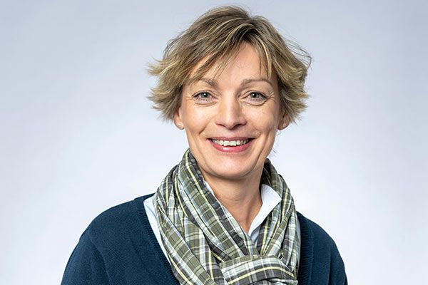 Eine Frau mit Schal und Pullover lächelt in die Kamera.