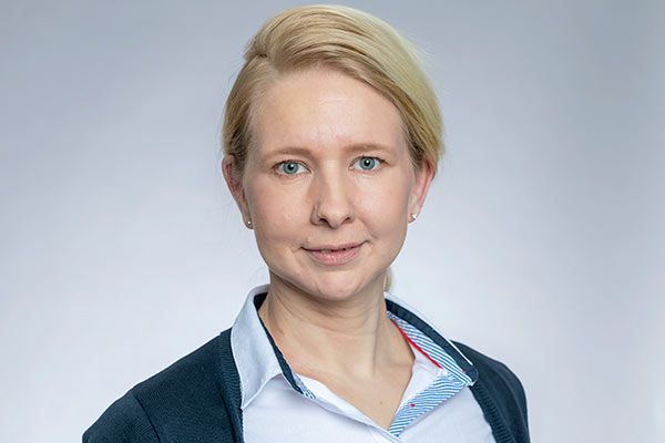 Eine Frau in einem weißen Hemd und einer schwarzen Jacke lächelt in die Kamera.