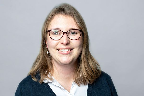 Eine Frau mit Brille und blauem Pullover lächelt in die Kamera.