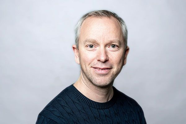 Ein Mann in einem blauen Pullover lächelt in die Kamera.