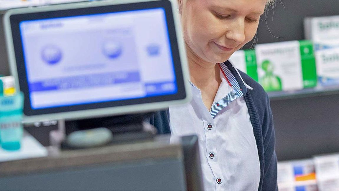 Eine Frau steht in einer Apotheke vor einem Computer.