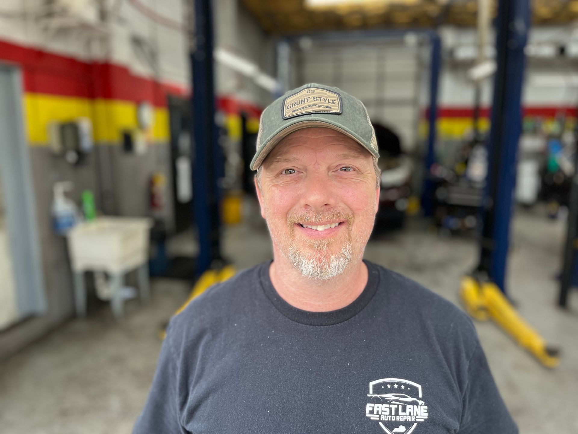 Man in garage wearing a cap and smiling, with car lifts in the background.