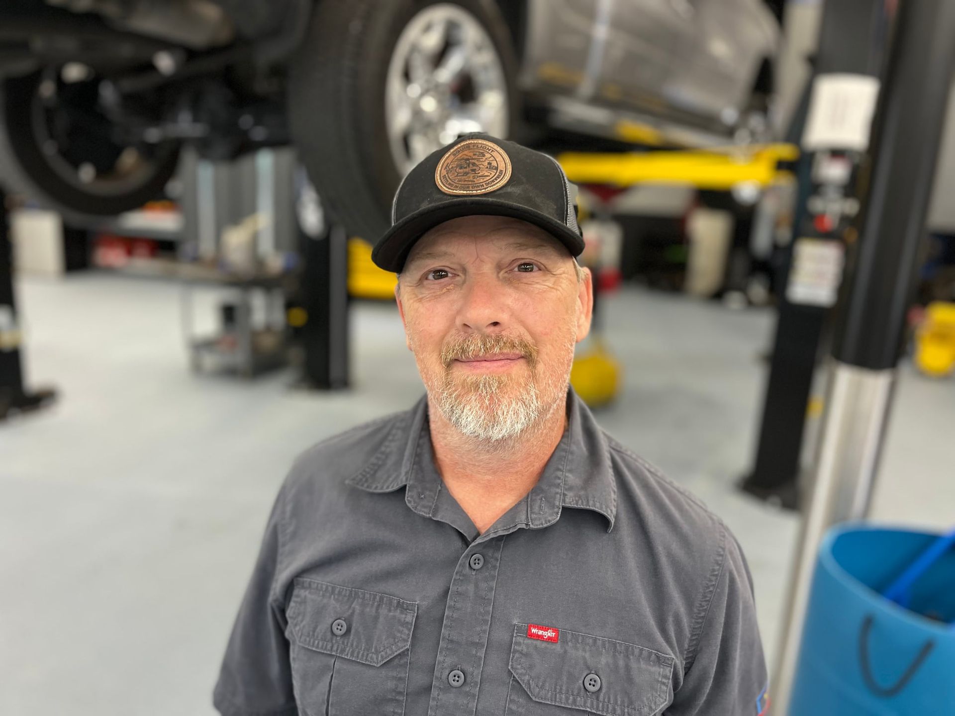 Man in garage wearing a cap and smiling, with car lifts in the background.