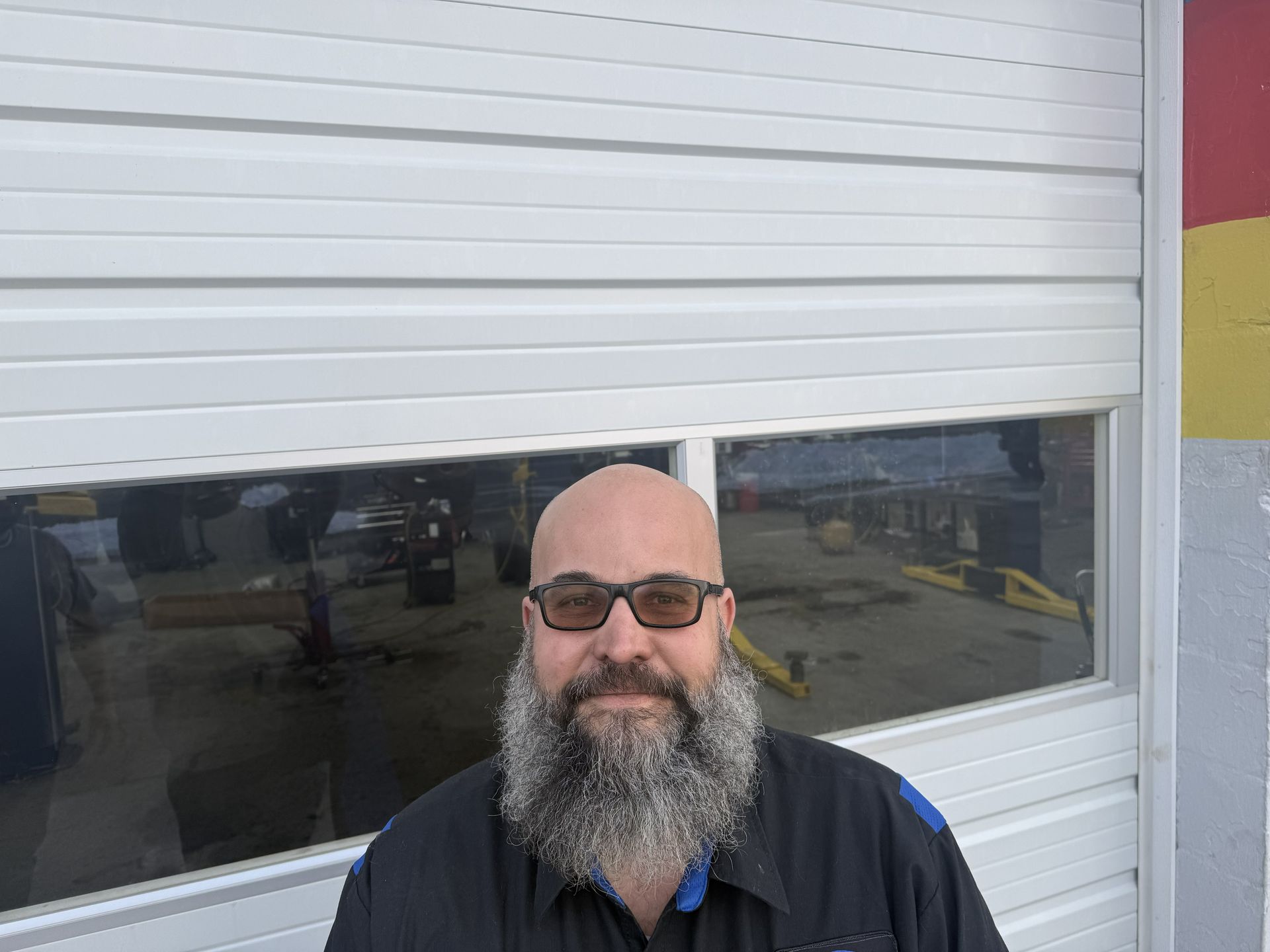 Man with a beard and sunglasses in front of a garage door.