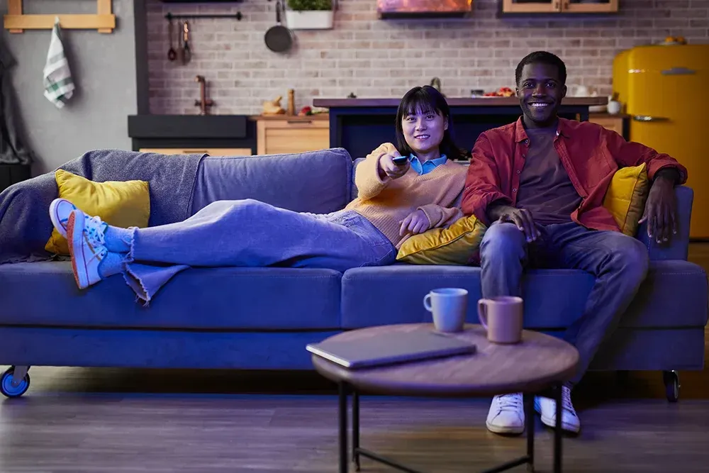 A man and a woman are sitting on a couch watching tv.