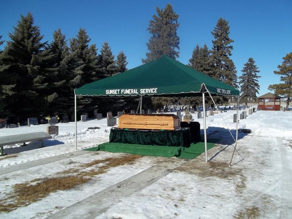 A casket on a green platform under a tent at a snowy cemetery.
