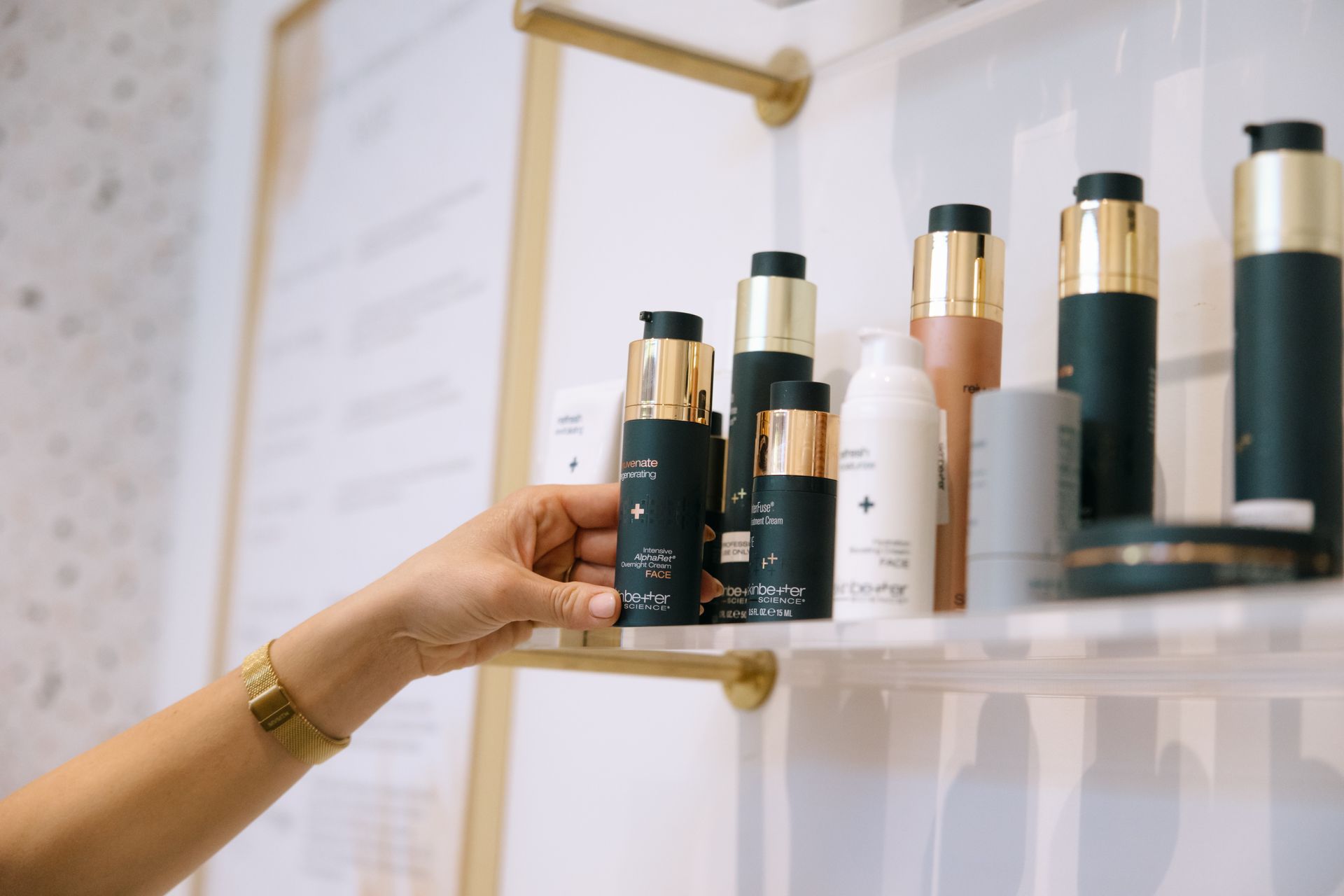 Woman's hand reaching for a skincare bottle on a shelf in a store.