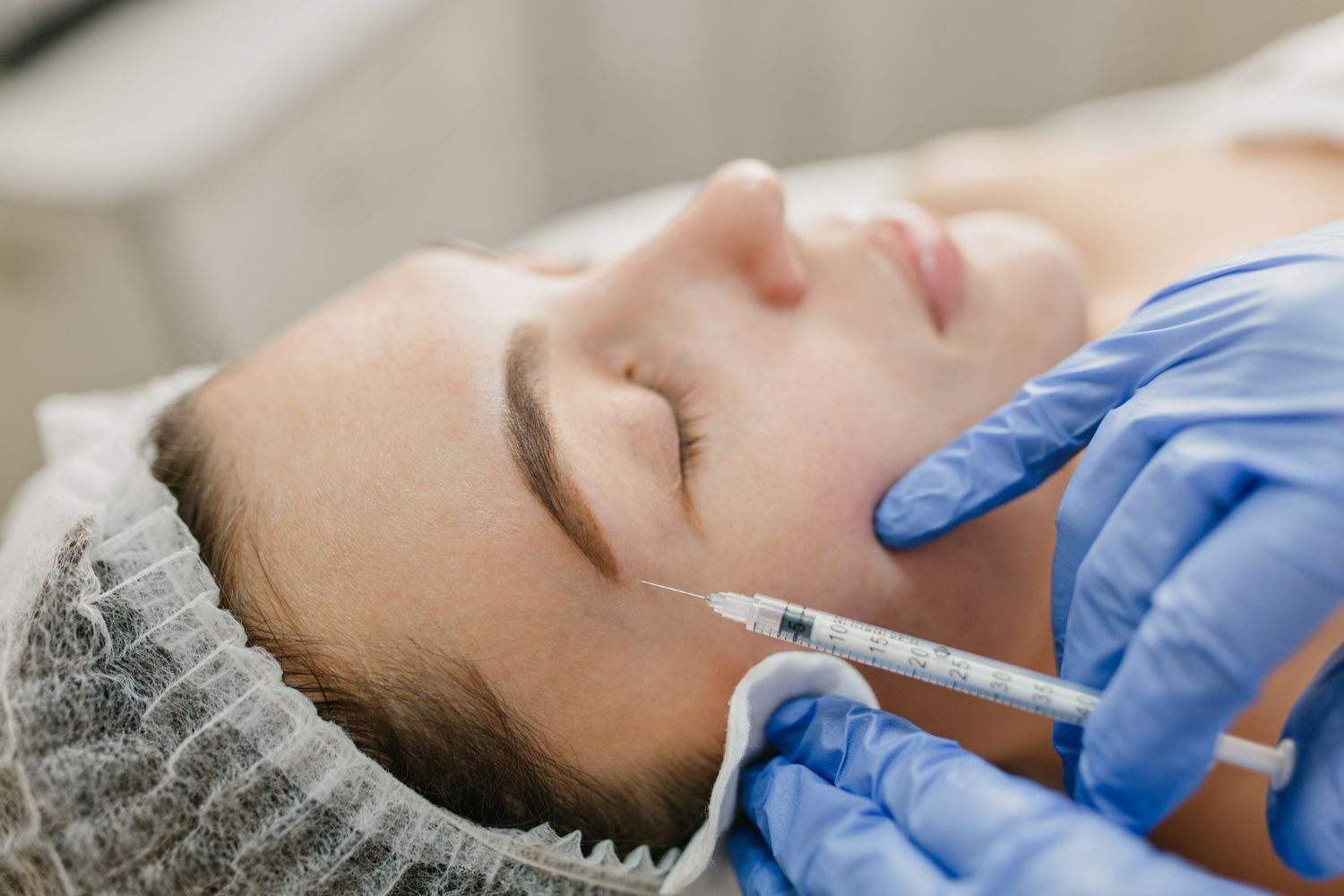 Woman receiving an injection on her forehead; medical professional in blue gloves.