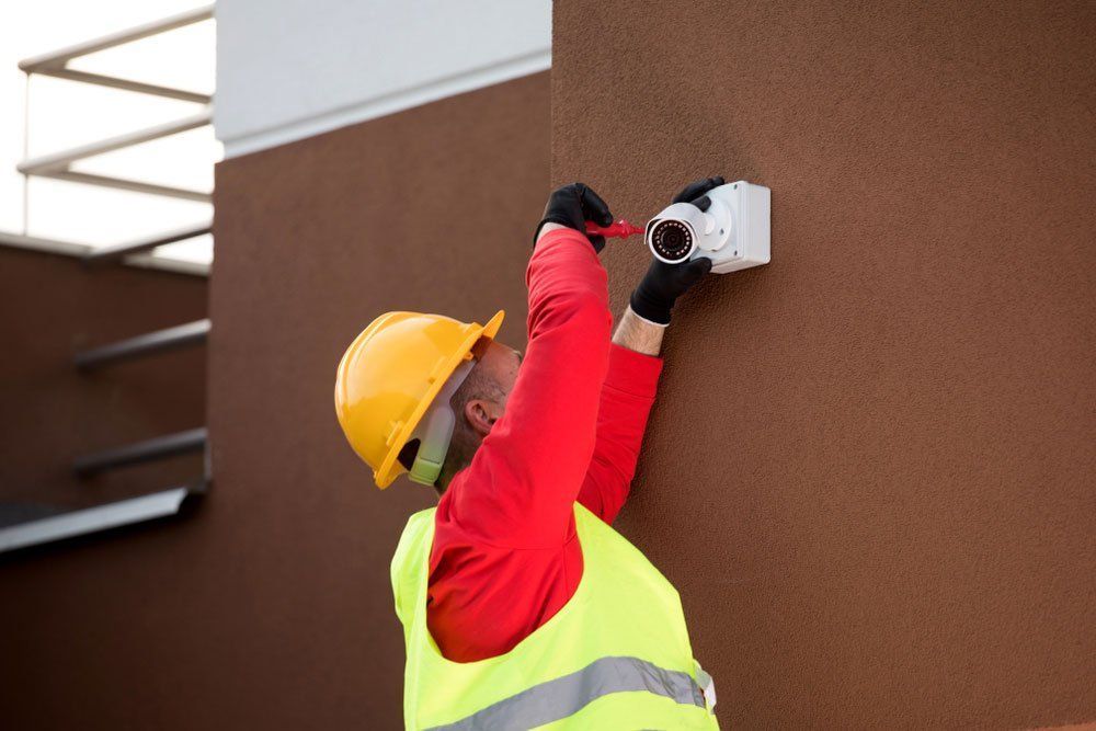 A Man Is Installing A Security Camera On The Side Of A Building — Country to Coast Cabling in Yeppoon, QLD