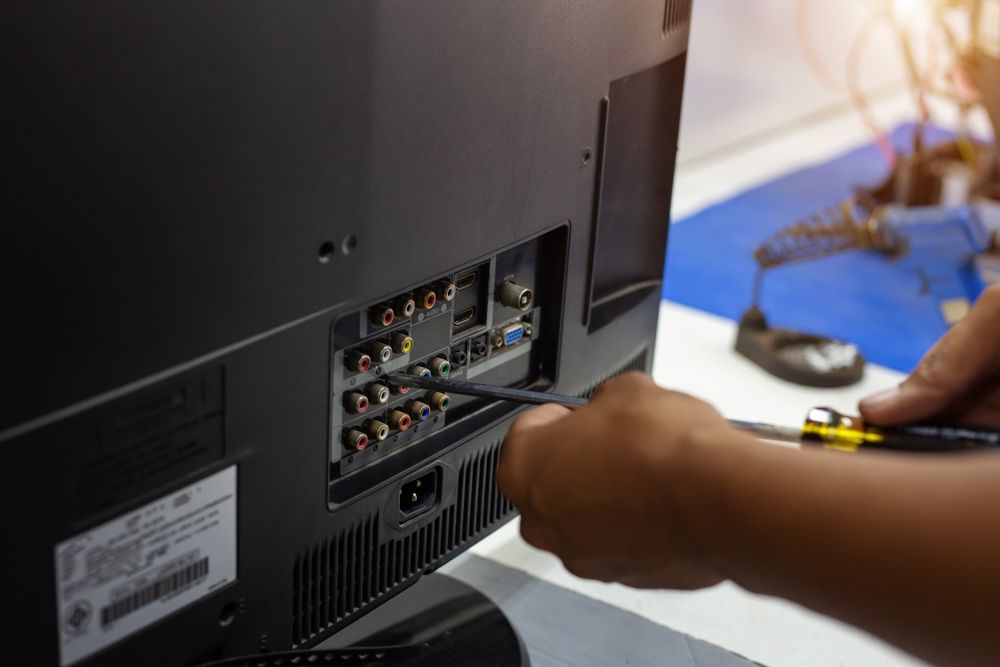 A Person Is Fixing A Television With A Screwdriver — Country to Coast Cabling in Kawana, QLD