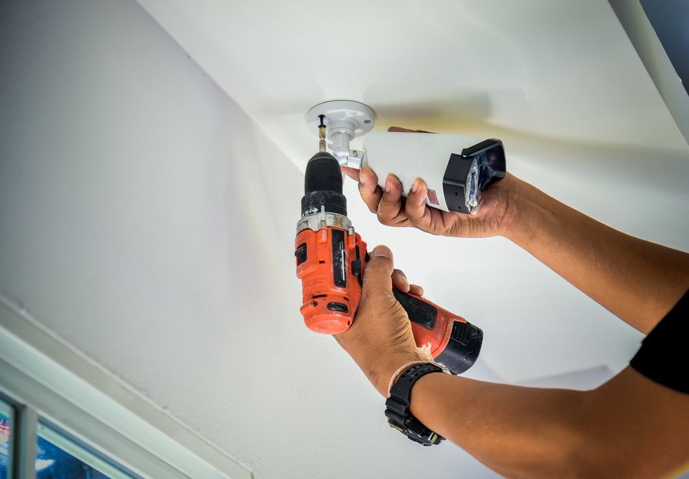 A Man Is Installing A Security Camera On A Wall With A Screwdriver — Country to Coast Cabling in Rockhampton, QLD