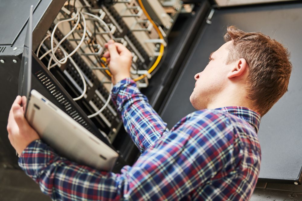 A Man In A Plaid Shirt Is Working On A Server — Country to Coast Cabling in Kawana, QLD