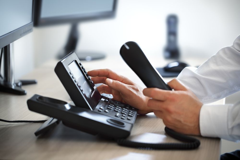 A Man Is Typing On A Telephone While Sitting At A Desk — Country to Coast Cabling in Kawana, QLD