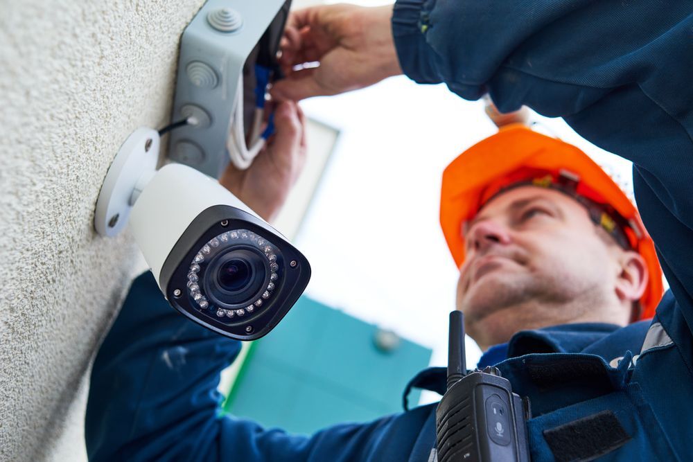 A Man Is Installing A Security System On A Brick Wall — Country to Coast Cabling in Rockhampton, QLD