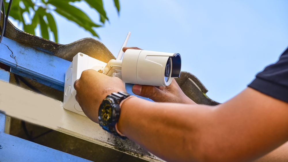 A Man Is Installing A Security Camera On A Roof — Country to Coast Cabling in Kawana, QLD