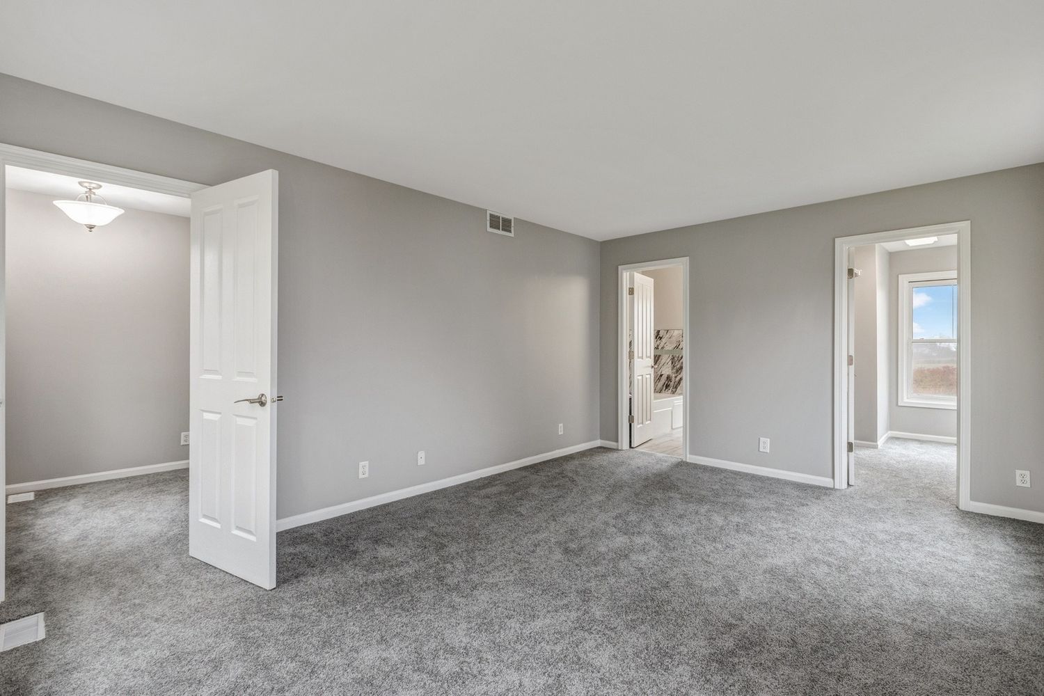 Empty bedroom with gray walls and carpet; three doorways.