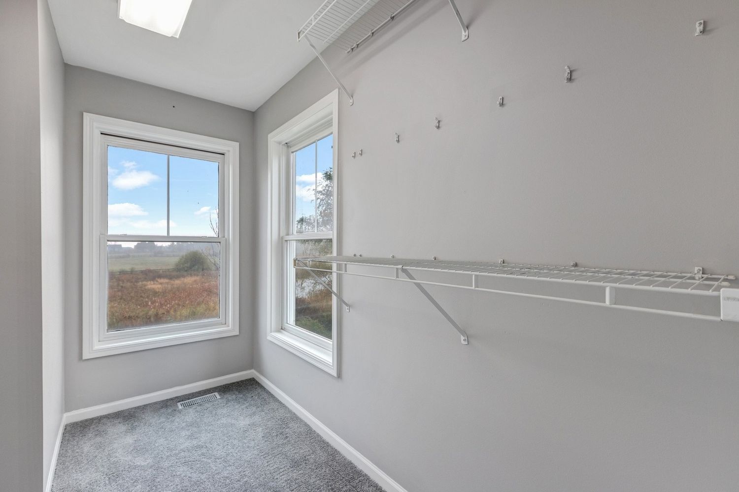 Empty walk-in closet with two windows, gray walls, and a wire shelf.