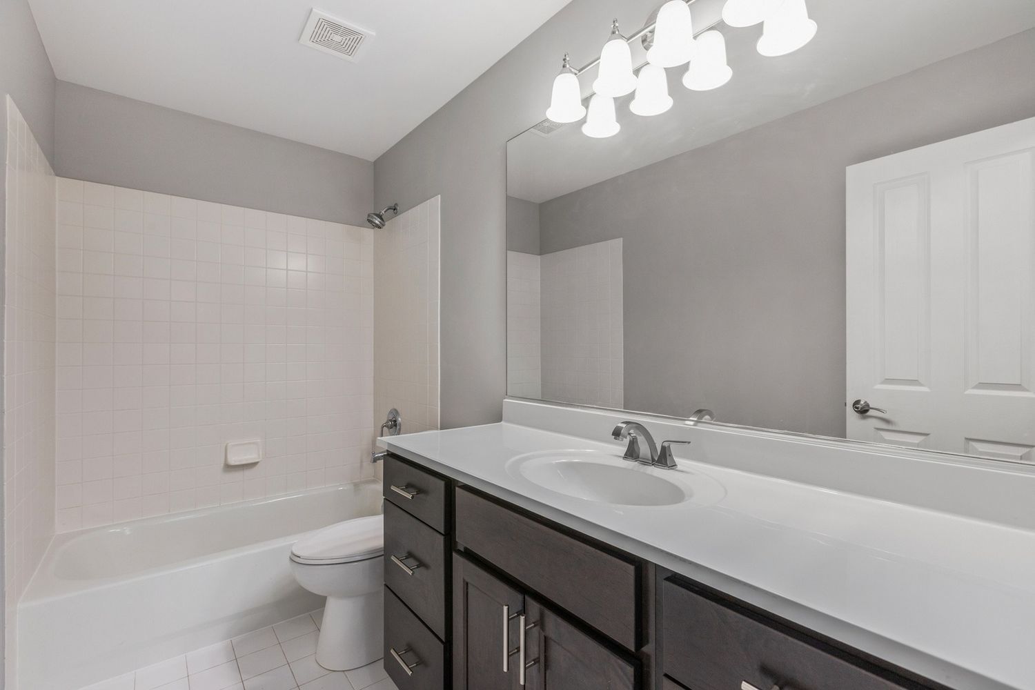 Bathroom with gray walls, white fixtures, dark cabinets, and a long mirror.