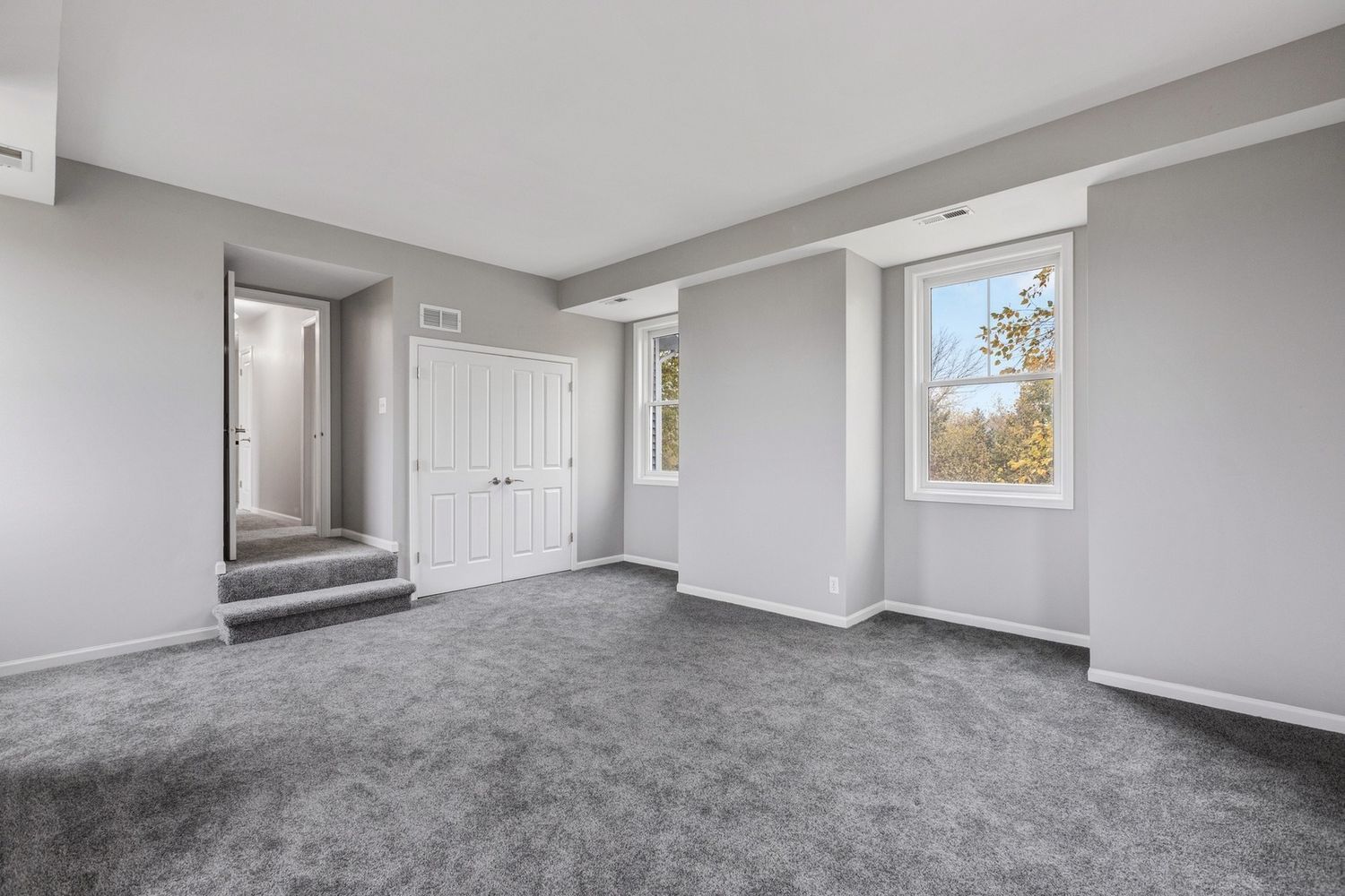Empty room with gray walls, carpet, and a white door and windows.