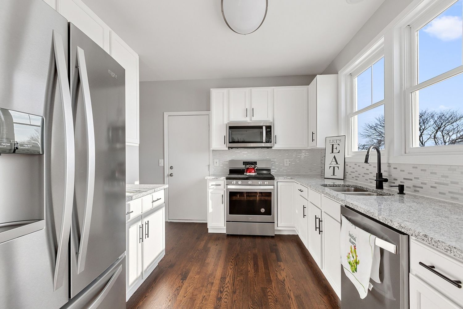 Bright white kitchen with stainless steel appliances, wood floor, and gray countertops.