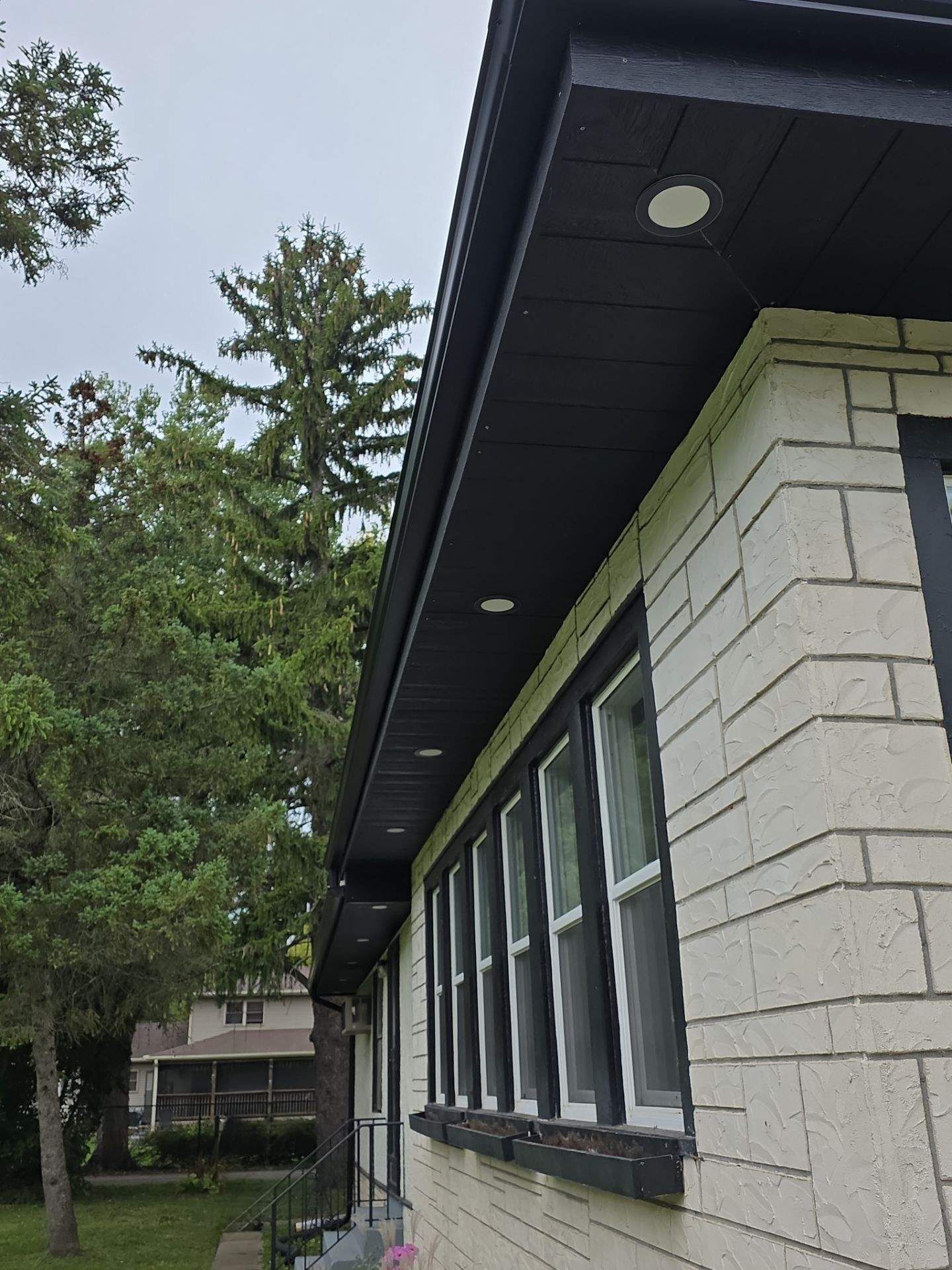 A side view of a cream-colored stone house exterior with black trim, black soffits, and recessed lighting.