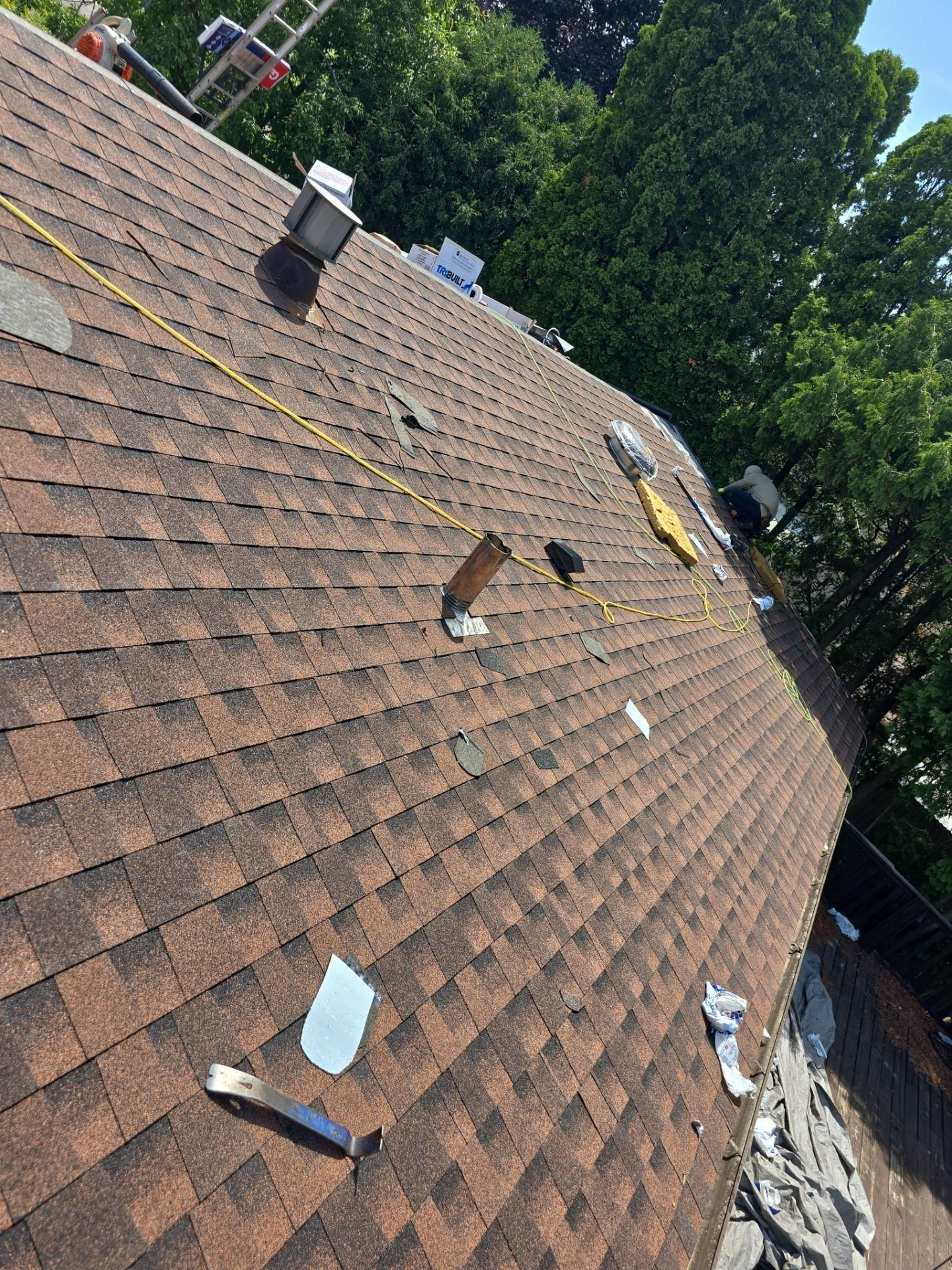 A high-angle view of a brown shingled roof under construction with tools, vents, and construction materials scattered.
