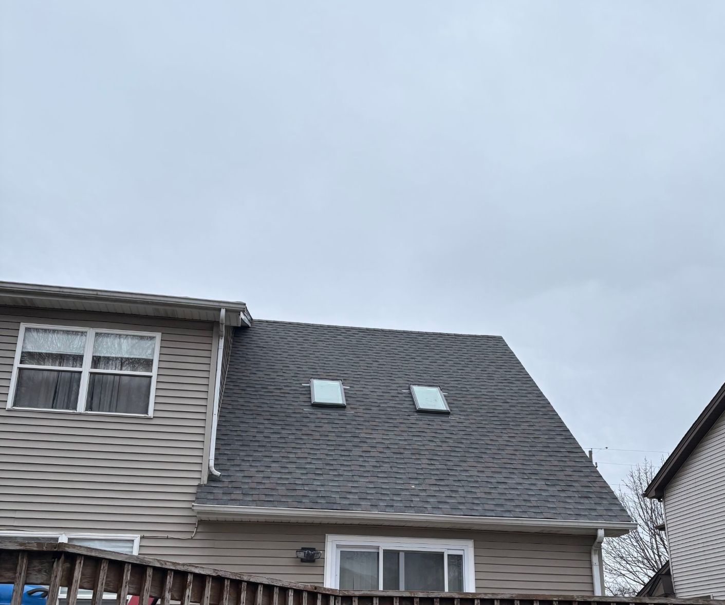 A two-story house with beige vinyl siding and a dark gray shingled roof featuring two small skylights.