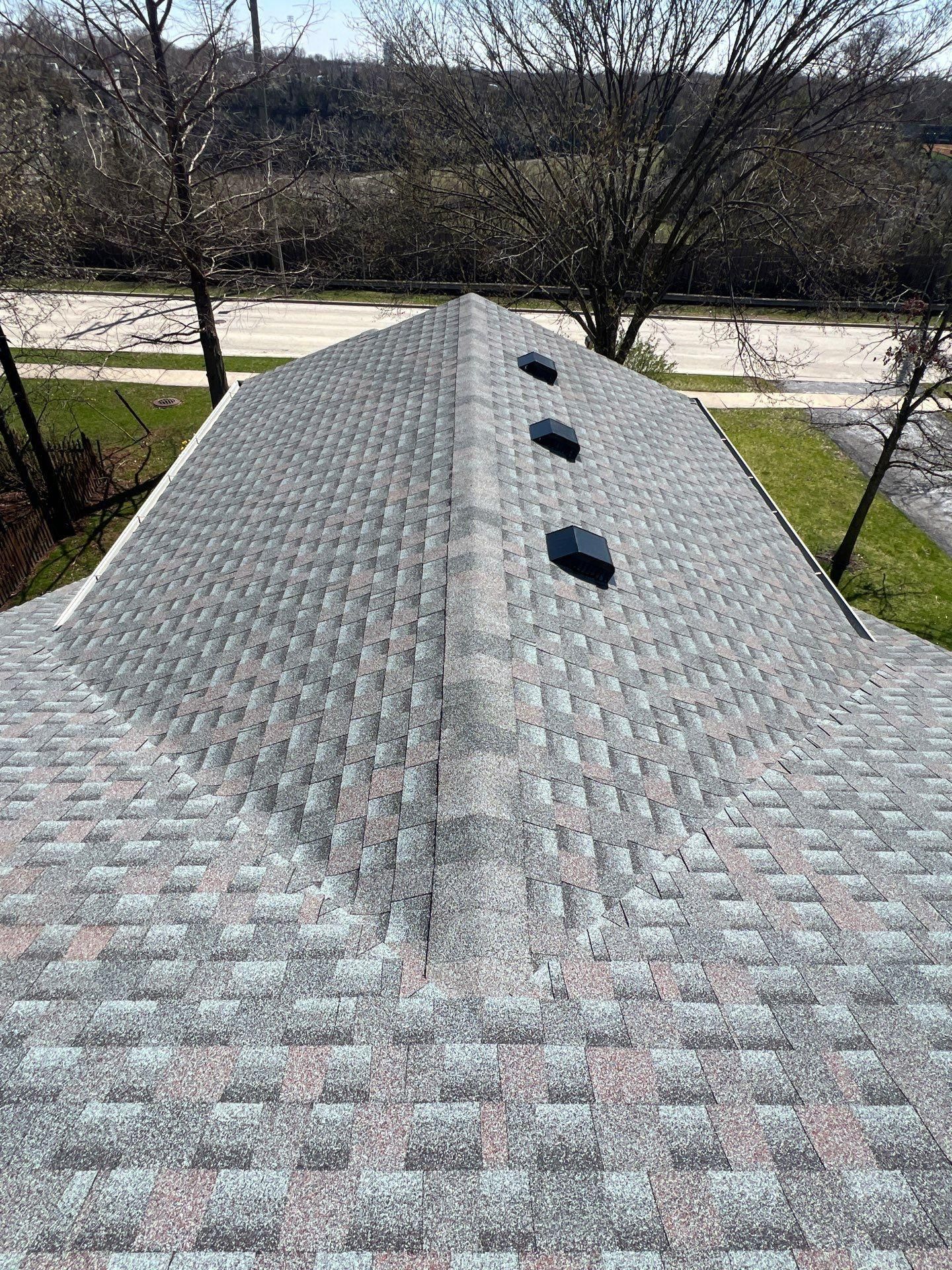 A high-angle view of a gray shingled residential roof with three square vents along the ridge line.