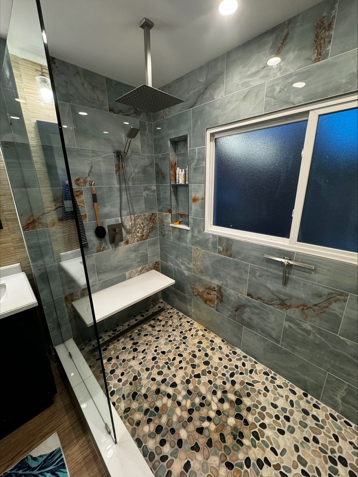 A walk-in shower with grey slate-look wall tiles, a pebble floor, a built-in bench, and a modern square rainfall showerhead.