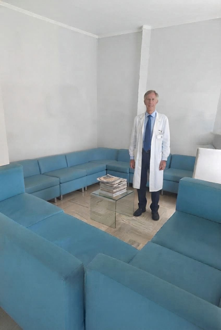 Un medico in piedi in una sala d'attesa con divani blu e un tavolino da caffè in vetro.