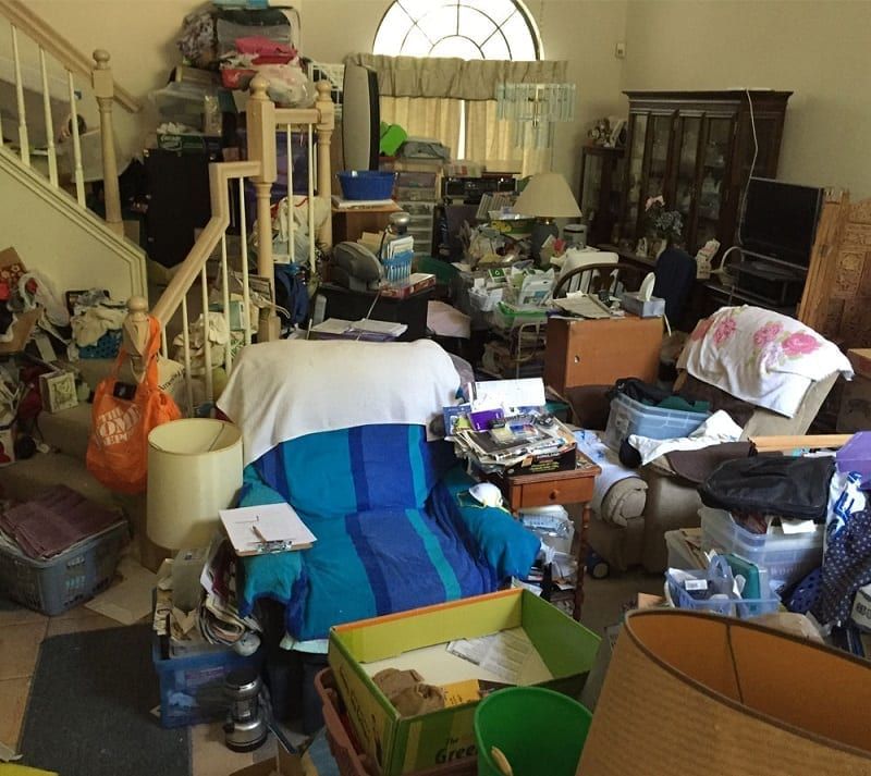 Living room with staircase and very full of clutter.