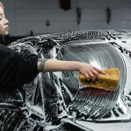 A woman is washing a car with a sponge.