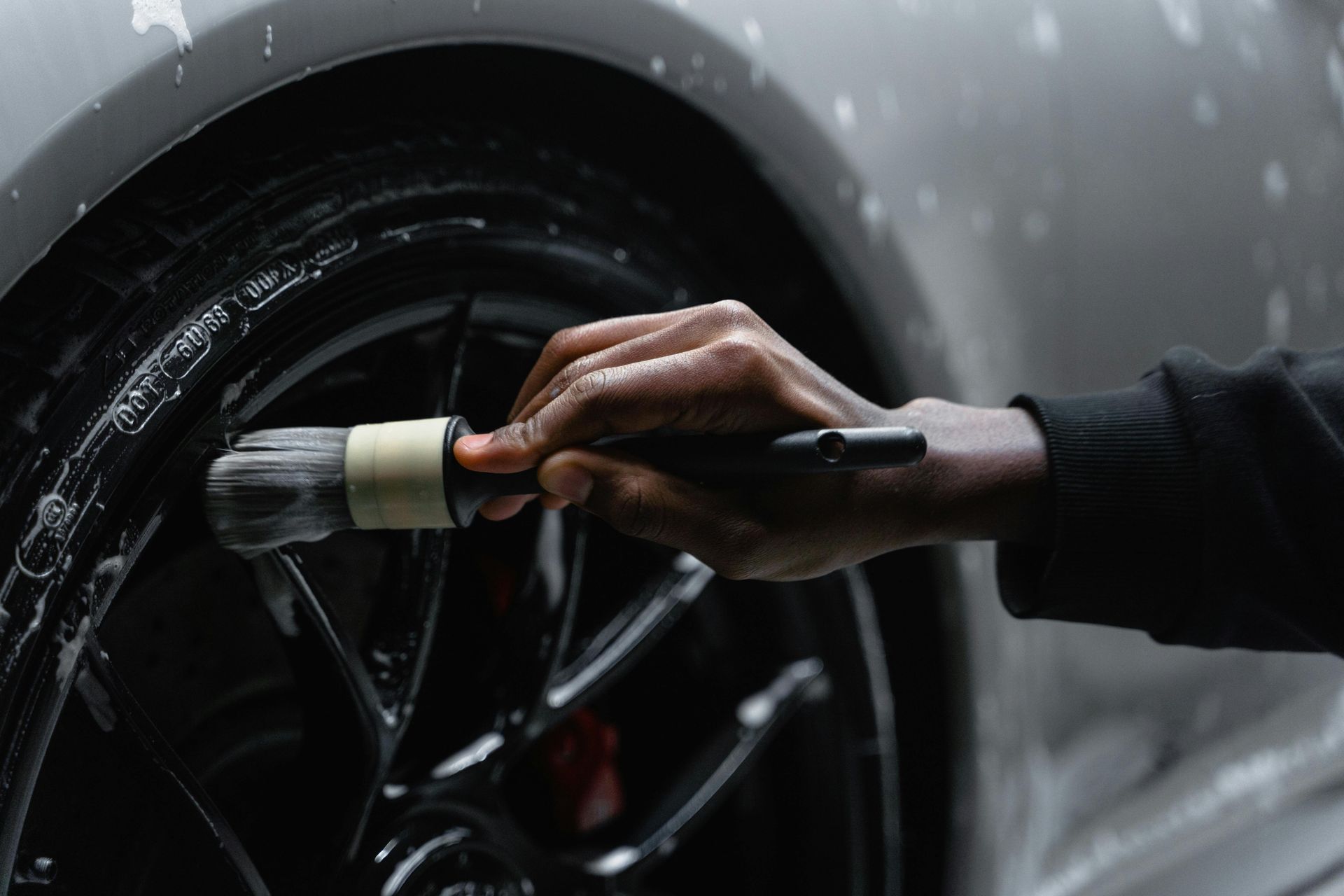 A person is cleaning a car wheel with a brush.