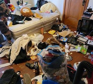 Un dormitorio con el suelo lleno de basura, ropa esparcida y un colchón con un peluche en un ambiente desordenado y oscuro.