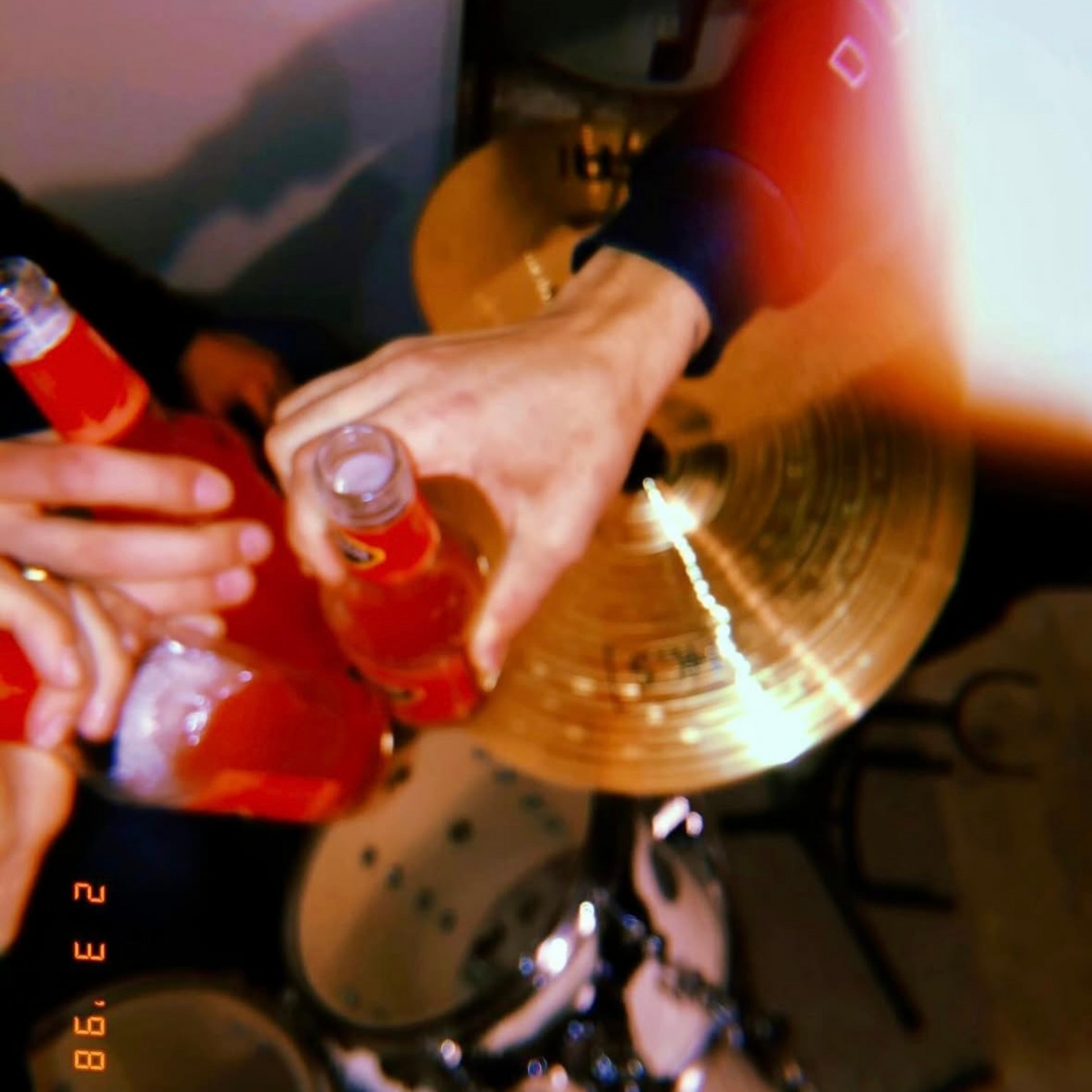 A person is holding a bottle of soda in front of a drum set