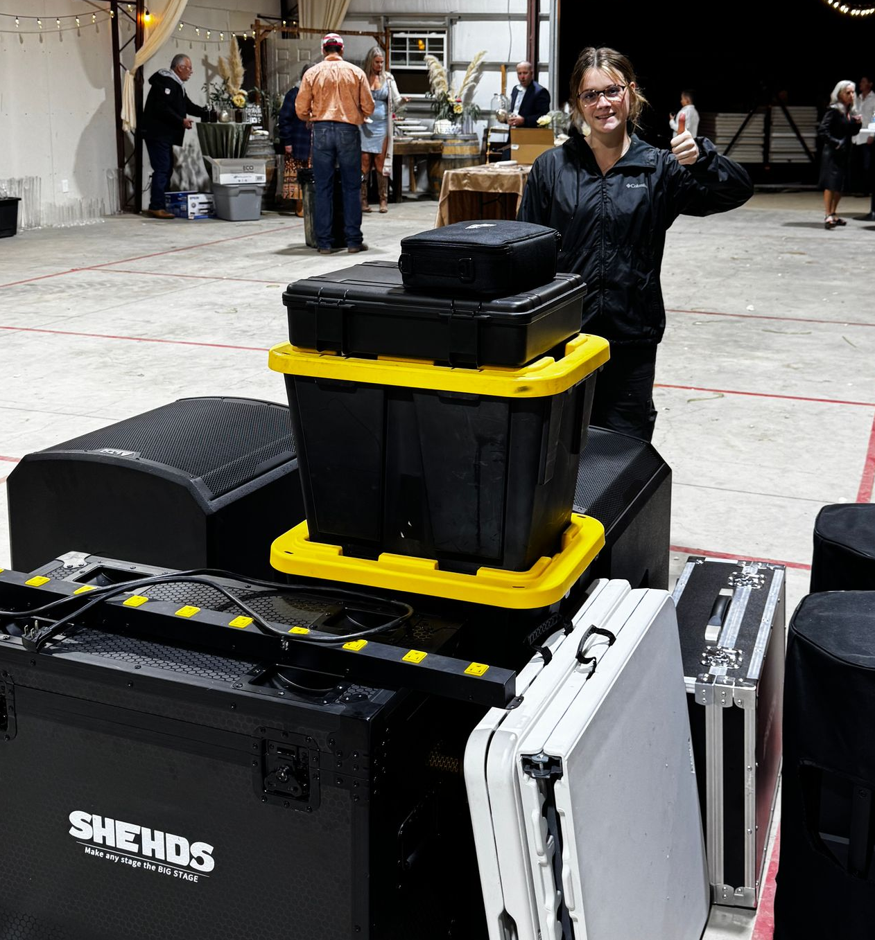 Woman stands by stacked black and yellow equipment cases in a warehouse-like room.