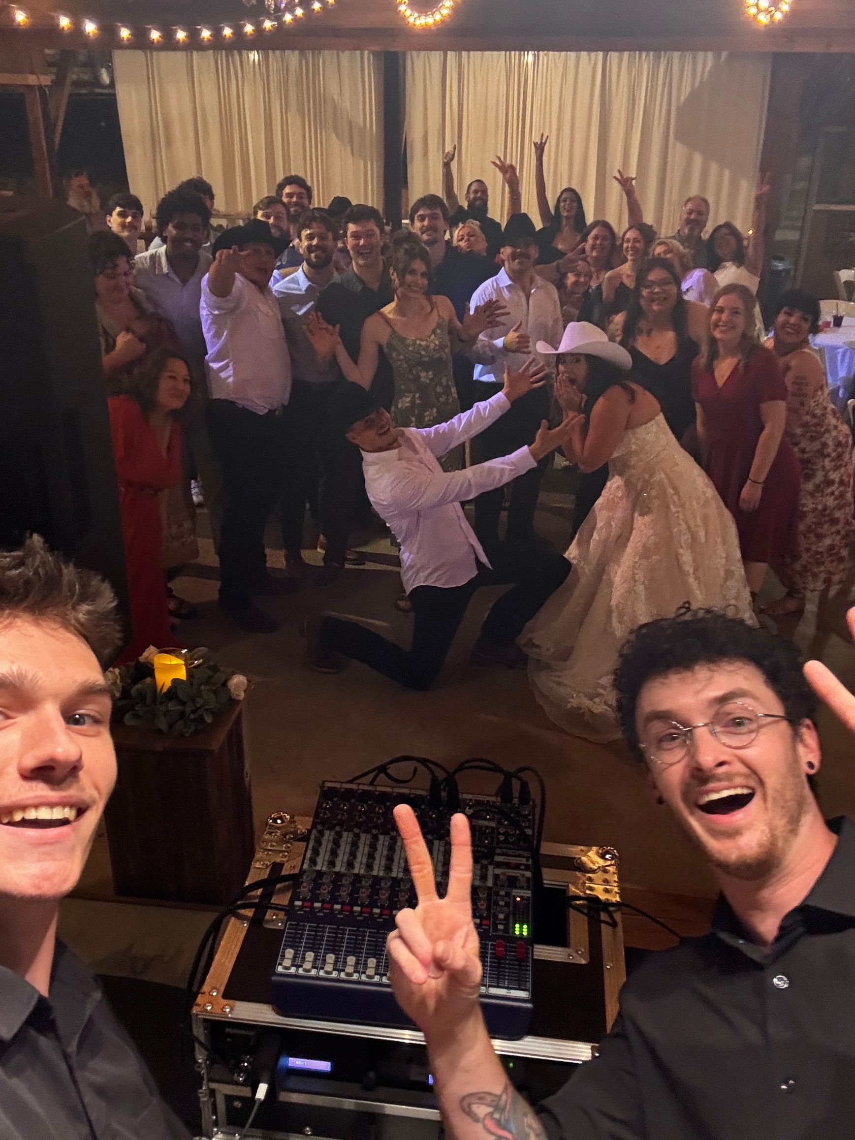 Crowded dance floor at a party, with two smiling DJ booth hosts in the foreground.
